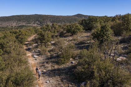 France, Herault, the Causses and the Cevennes, Mediterranean agro pastoral cultural landscape, listed as World Heritage by UNESCO, Saint Maurice Navacelles, hikers progressing on the GR 7 in a typical landscape of the Causse du Larzac, the Séranne massif which was formed on a coral reef in the background (aerial view)