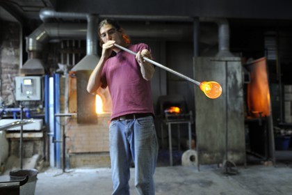 France, Moselle (57), Meisenthal, Thibaut souffleur au Centre international d’Art verrier (CIAV), fabrication d'une boule de Noël en verre. Tout en tournant la canne, il souffle dans la canne