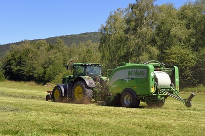 France, Puy-de-Dôme (63), Saint-Ours-les-Roches, hameau de Beauregard, tracteur récoltant le fourrage avec une presse enrubanneuse de balles de foin dans un champ