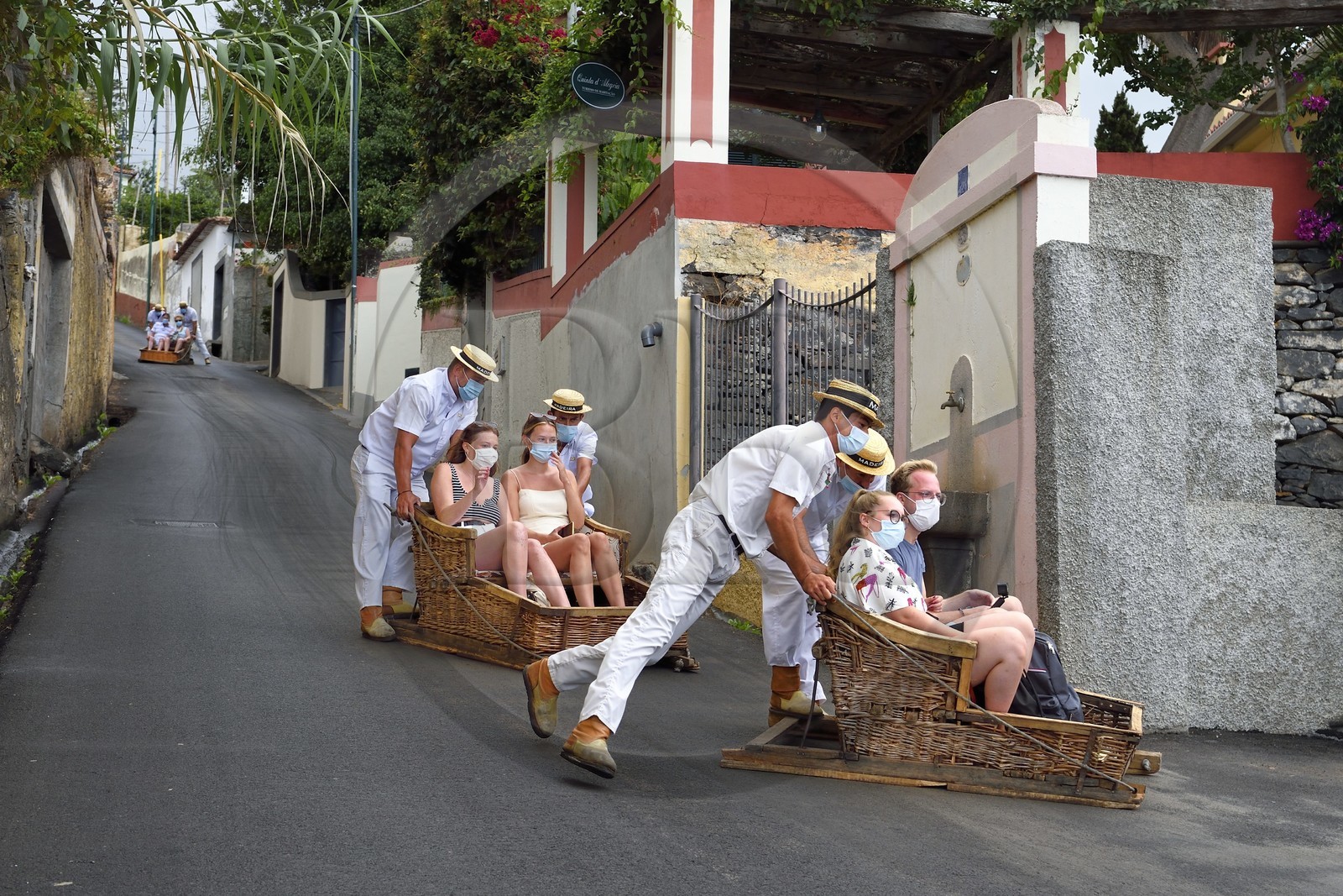 Portugal, Ile de Madère, Funchal, touristes effectuant la descente depuis le jardin tropical en traditionnel panier d'osier sur la route camino do Monte