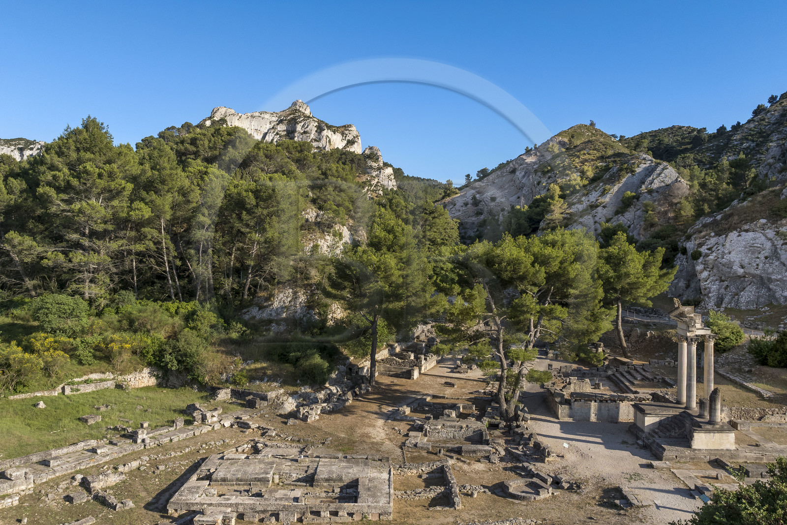 France, Bouches-du-Rhône (13), Parc Naturel Régional des Alpilles, Saint-Rémy-de-Provence, site archéologique de Glanum au pied du massif des Alpilles, colonnes et entablement reconstitués du petit temple géminé du premier forum au premier plan à droite (vue aérienne)