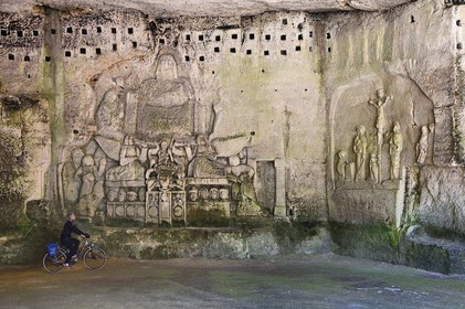 France, Dordogne (24), Brantôme, l'abbaye bénédictine Saint-Pierre de Brantôme, vestiges du premier monastère troglodytique aménagé dans les grottes au pied de la falaise avec notamment dans la grotte du Jugement Dernier, à droite la Crucifixion du début XVIIème siècle, à gauche un bas relief du XV ème siècle sous le pigeonnier, cycliste sur la véloroute la Flow Vélo