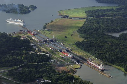 Panama, Colon province, Panama Canal, Gatun locks, Panamax cargo passing the locks, a cruise ship on Gatun Lake in the background (aerial view)