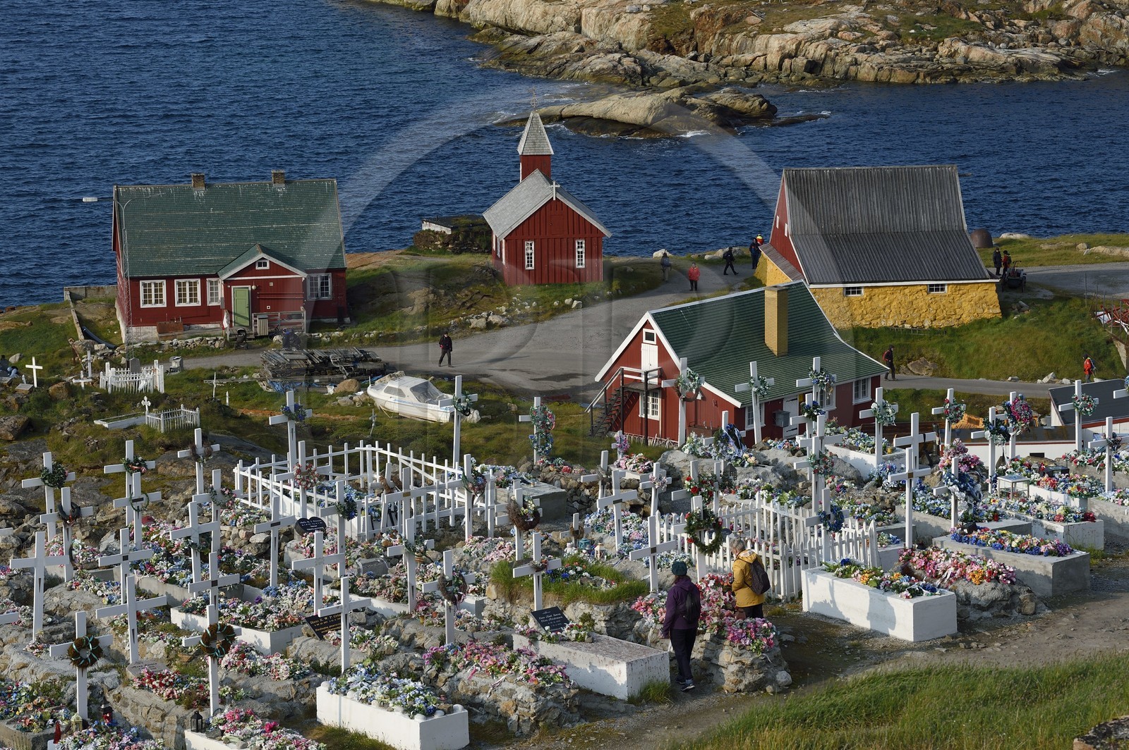 Groenland, cote ouest, baie de Baffin, Upernavik, le cimetière, les cercueils sont déposés en surface puis recouverts de pierres ou de ciment, le sol ne pouvant être creusé, les tombes sont ensuite décorées avec des fleurs artificielles, l'ancienne église et les batiments du musée en arrière plan