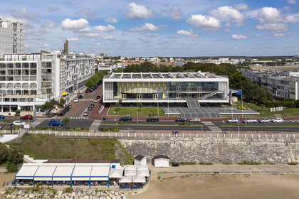 France, Charente-Maritime (17), Royan, le Palais de congrès (1957) signé de l’architecte-urbaniste Claude Ferret et rythmés par les panneaux perforés en aluminium jaune et gris des ateliers Jean Prouvé en façade, l'église Notre-Dame de Royan construite de 1955 à 1958 par l'architecte Guillaume Gillet en arrière plan (vue aérienne)